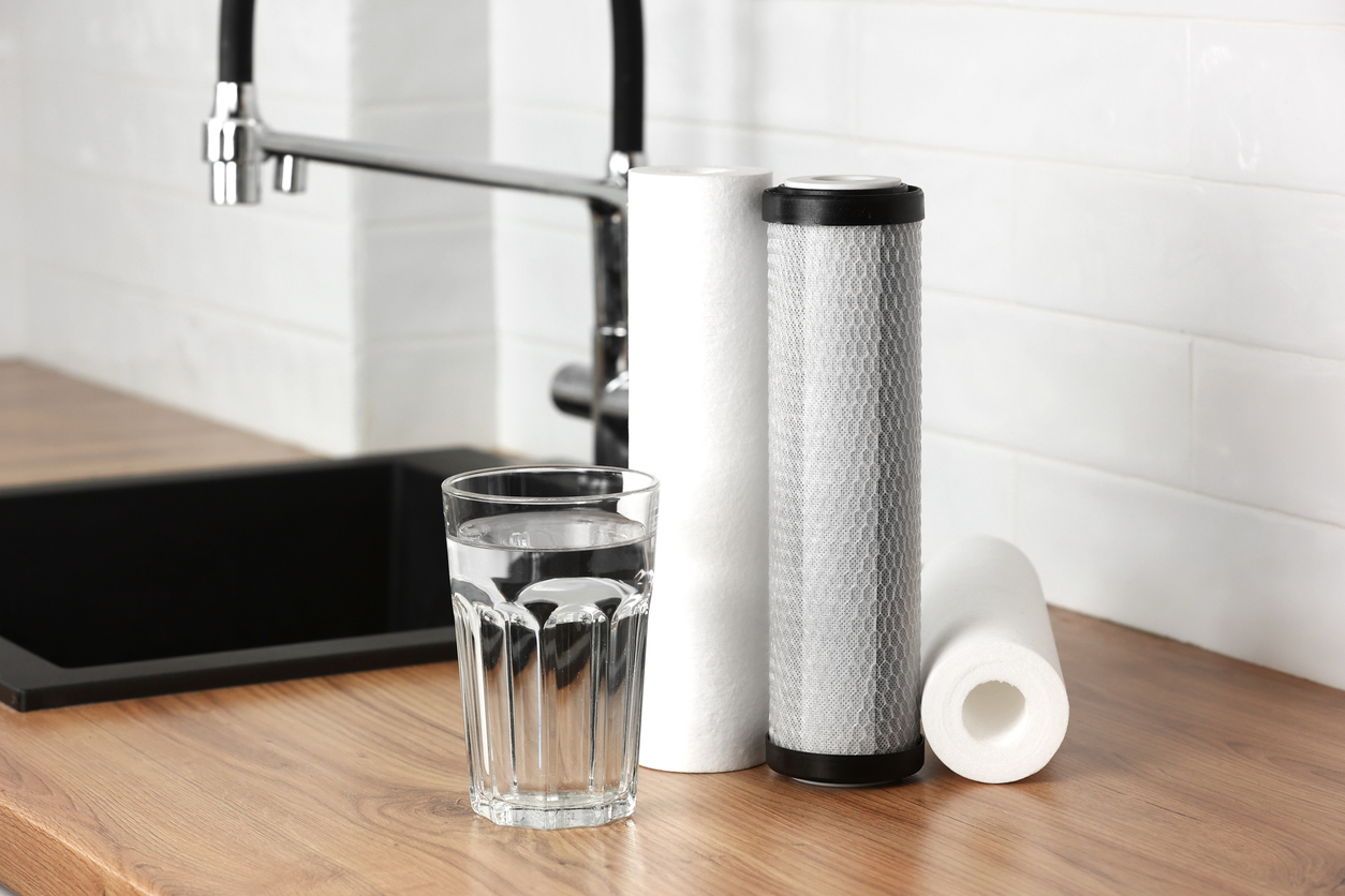 A glass of clean fresh water and set of filter cartridges on wooden table in a kitchen interior.