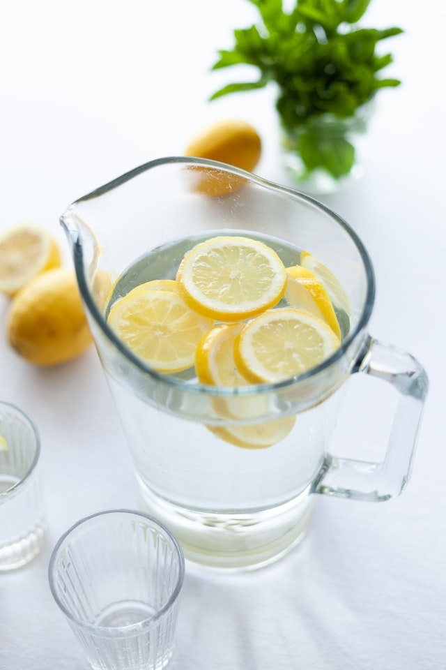 Clear glass pitcher filler with clear liquid and slices of lemon