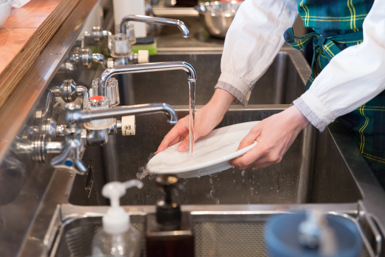 lady washing a plate on a stainless steel basin.